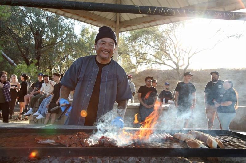 Fotografía cedida por Randall Michaelson, a través de KCET, donde aparece el chef Roy Choi mientras sonríe junto a una parrilla al estilo latinx en Chavez Ravine de Los Ángeles, California. EFE/Stephen Vanasco
