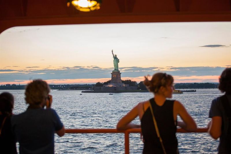 Fotografía cedida este miércoles por NYC & Company donde aparecen unas personas mientras observan la Estatua de la Libertad mientras viajan en un ferri, en Nueva York (Estados Unidos). 