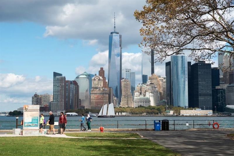 Fotografía cedida este miércoles por NYC & Company donde aparecen unas personas mientras pasean en Governors Island, frente a los rascacielos de Nueva York (Estados Unidos).